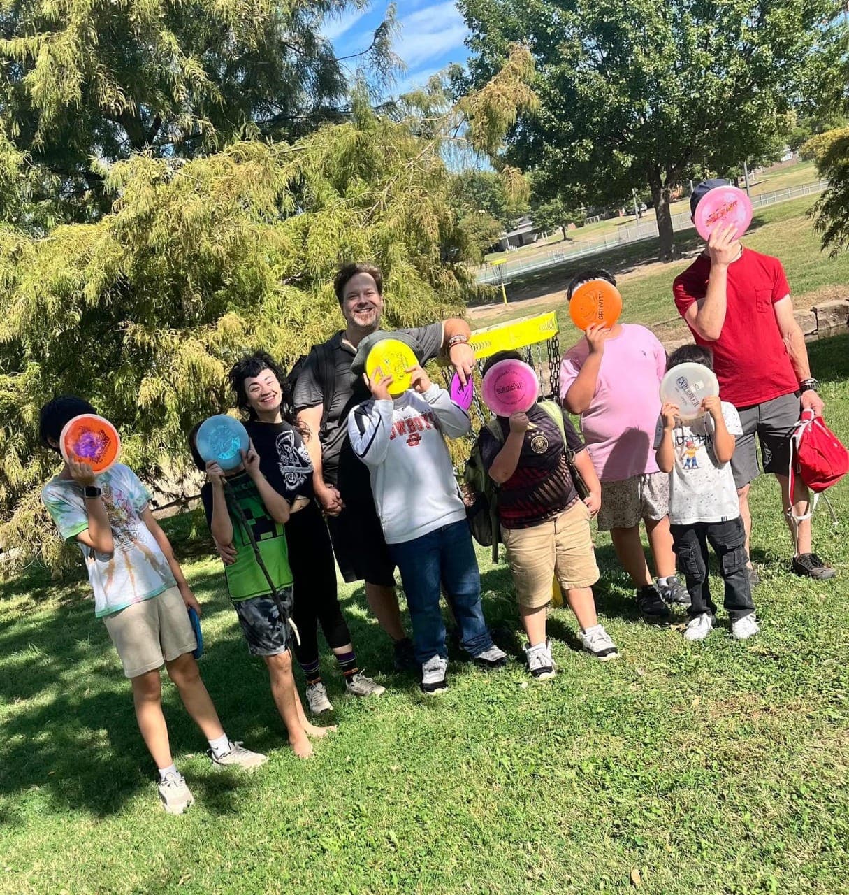 Sol Vibrations mentors and kids hold colorful discs in front of their faces at a park outing