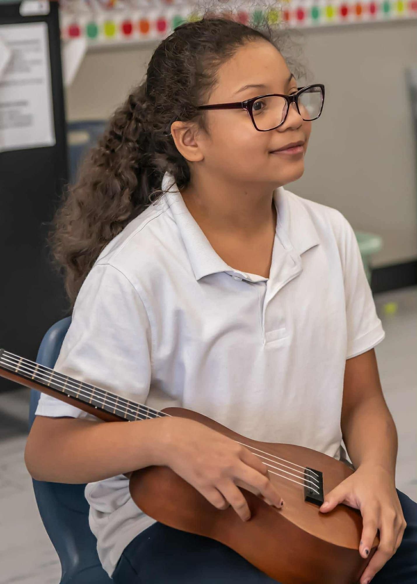 A student smiles while cradling her ukulele