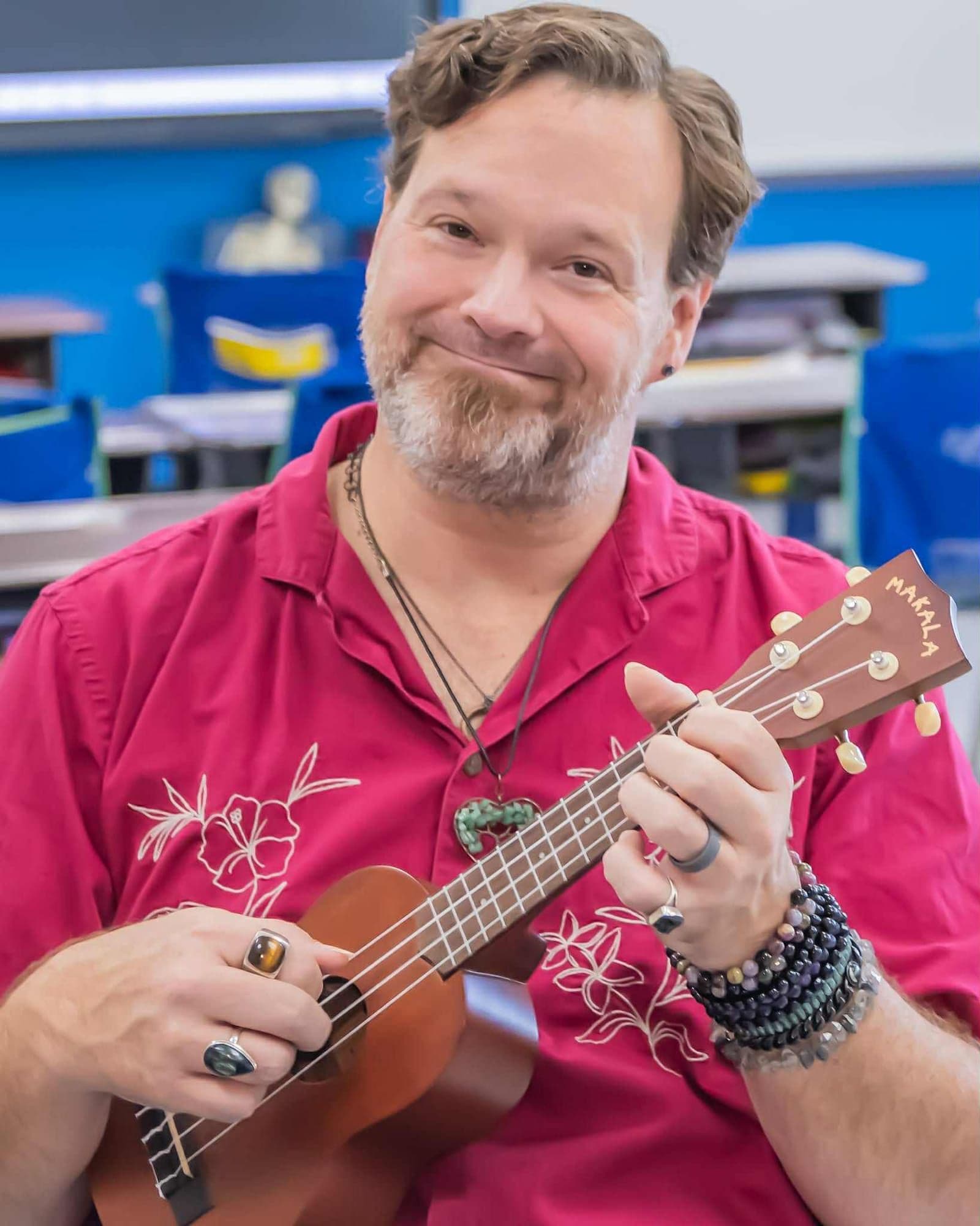 John Ford smiles while holding his ukulele in a classroom
