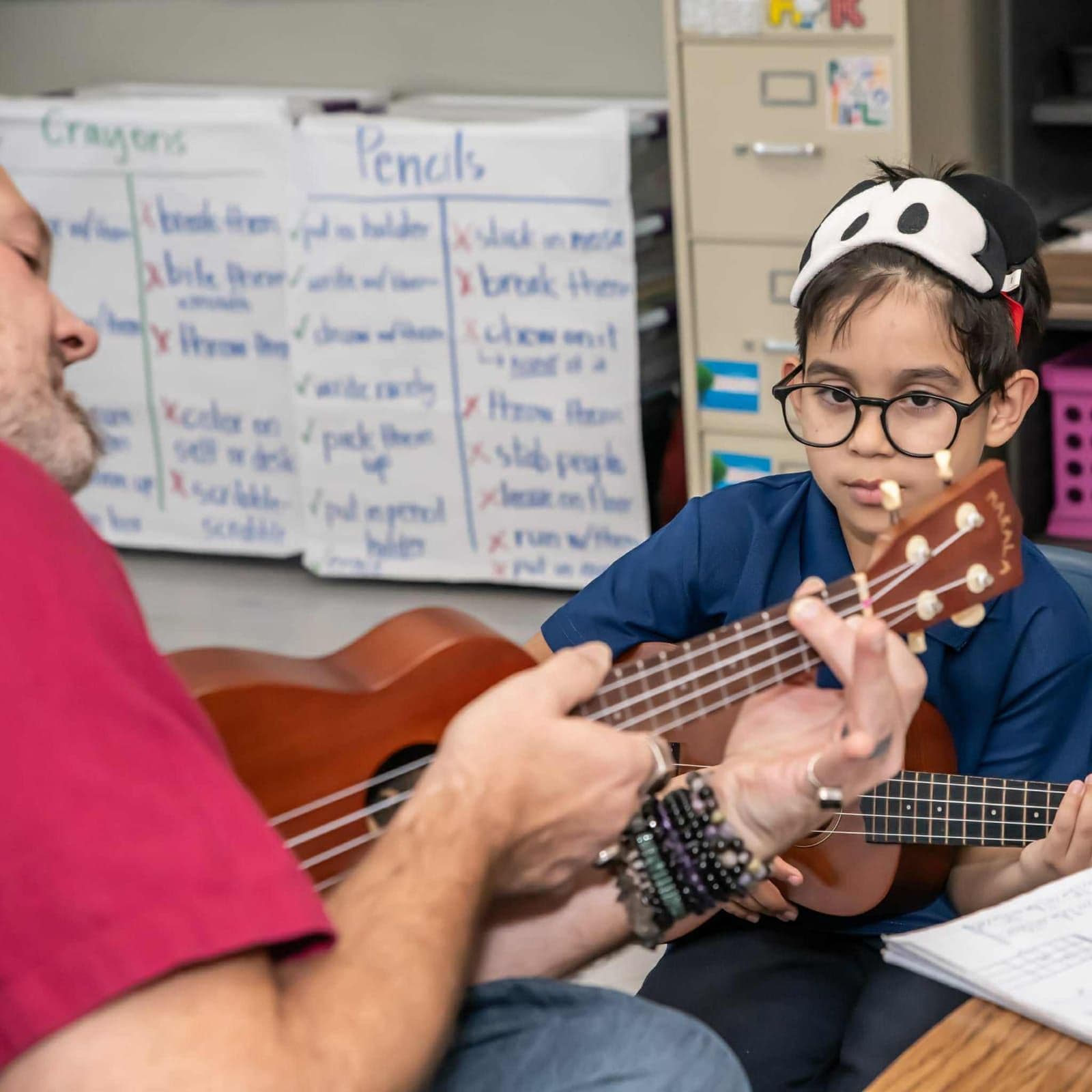 John Ford plays ukulele while a student watches his hands closely