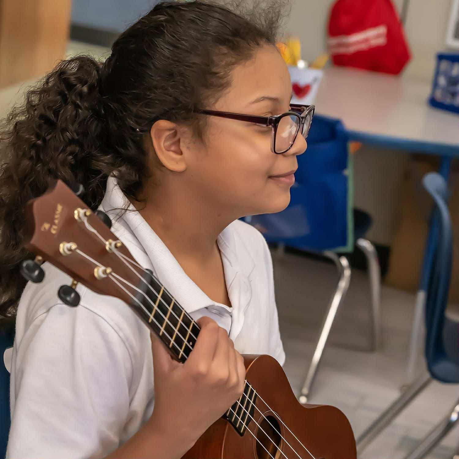 A smiling student in glasses holds a ukulele over her shoulder