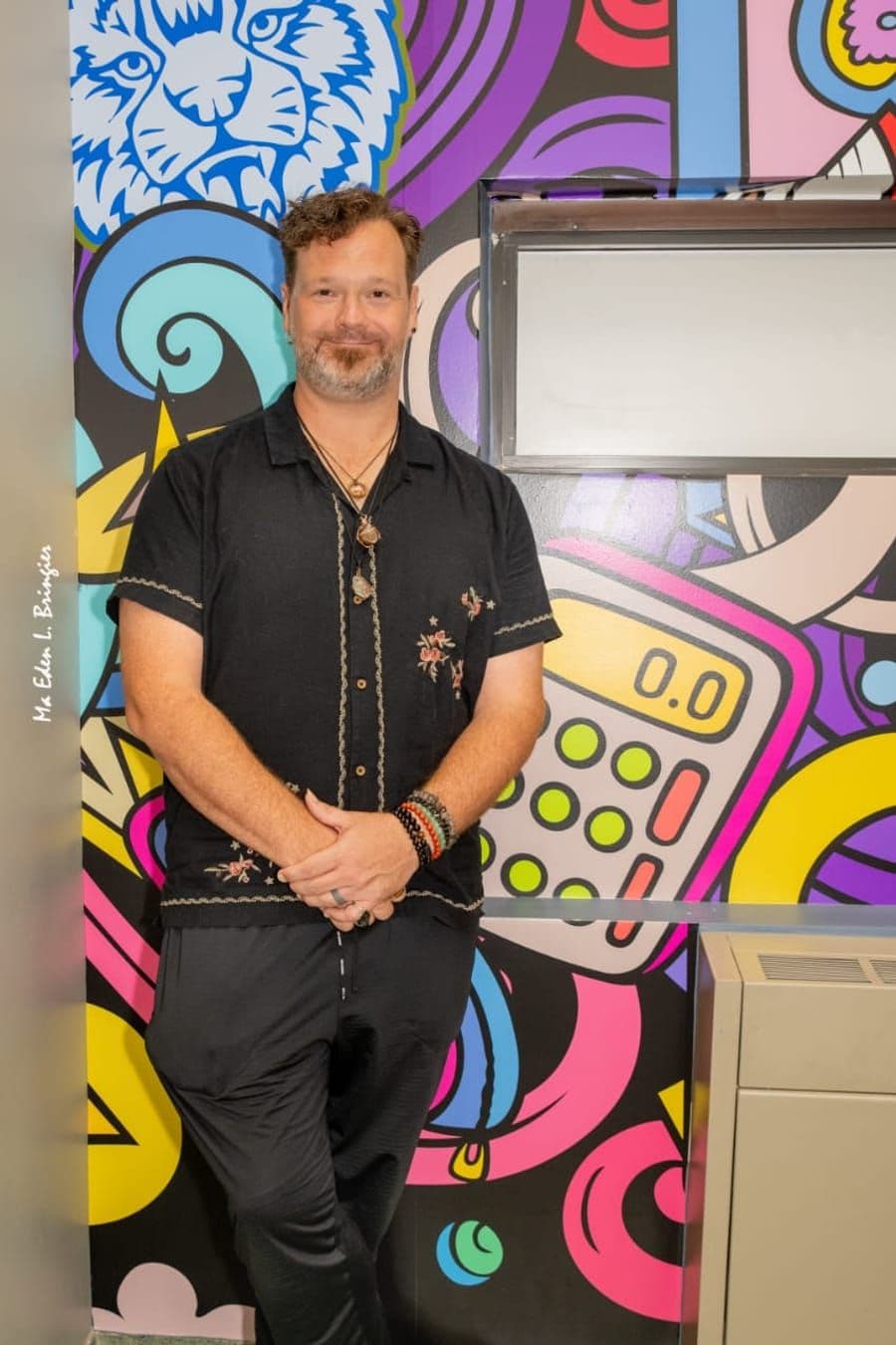 John Ford, co-founder of Sol Vibrations, standing in front of a colorful mural