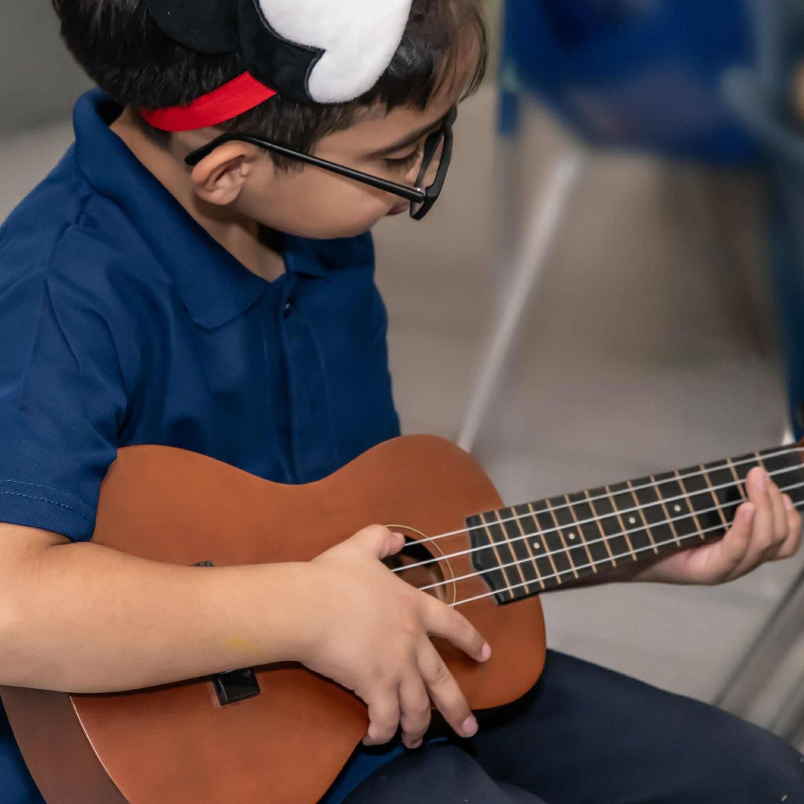 A young student in glasses strums a ukulele during a lesson